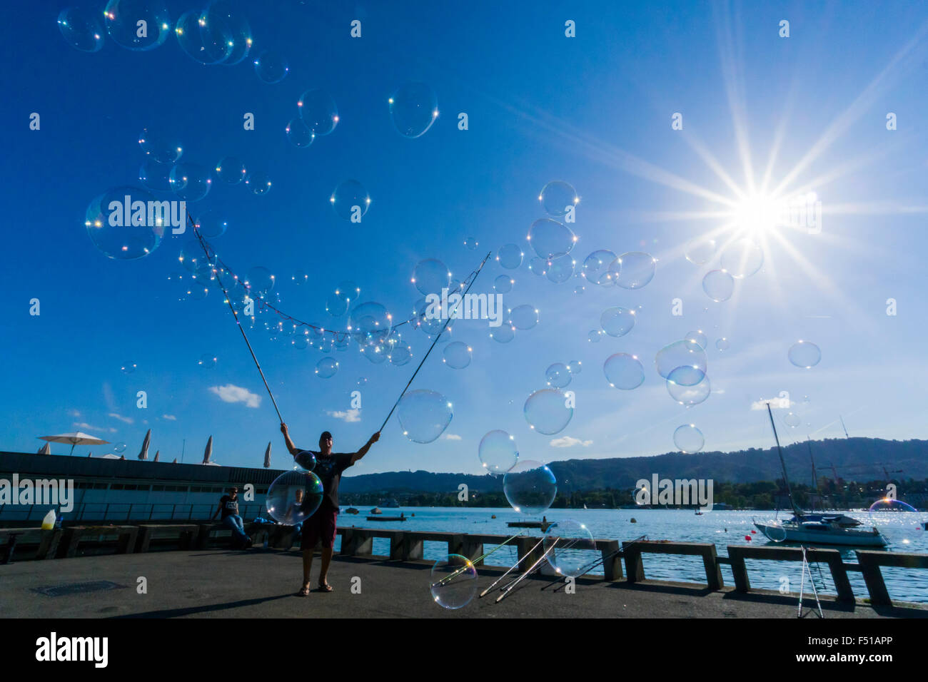 Un uomo è la creazione di un numero elevato di bolle a riva del lago zuerichsee, visto contro la luce del sole Foto Stock