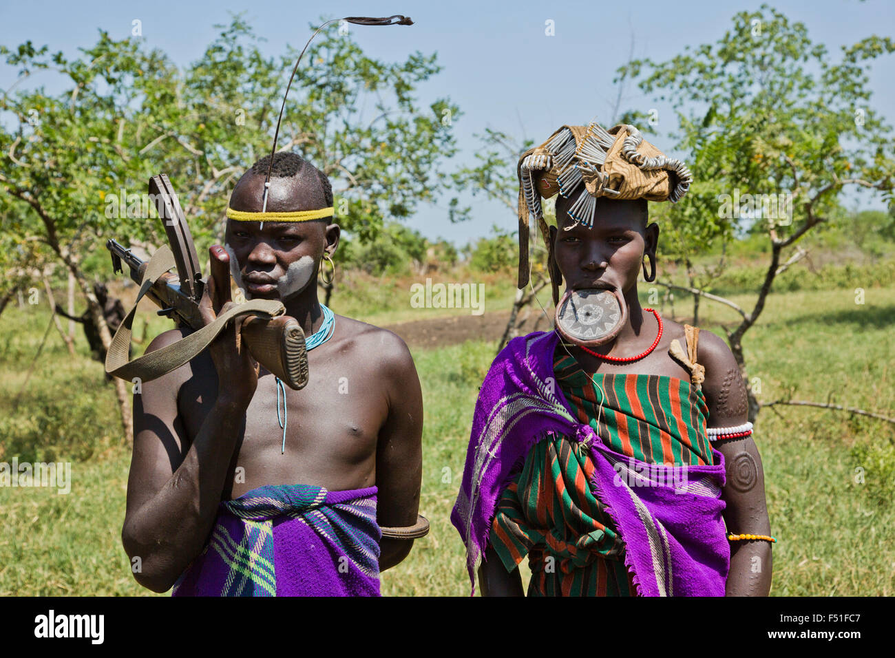 Tribù dei Mursi giovane donna ha un labbro di argilla disco come corpo ornamentstribe l uomo sta portando un AK-47 Debub Omo Zona, Etiopia. Cl Foto Stock