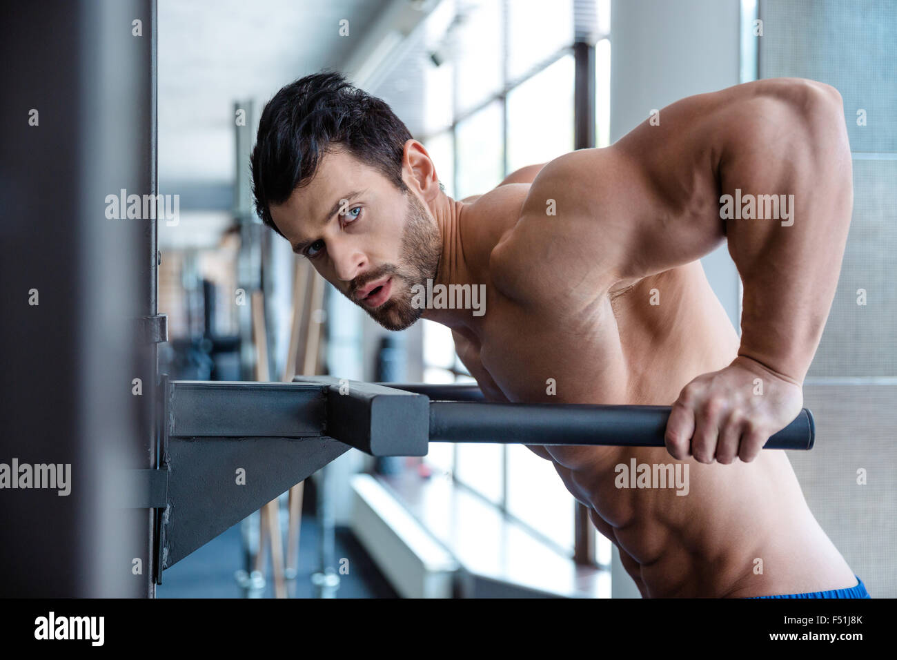 Ritratto di un uomo muscolare allenamento su barre parallele in palestra per il fitness e guardando la fotocamera Foto Stock