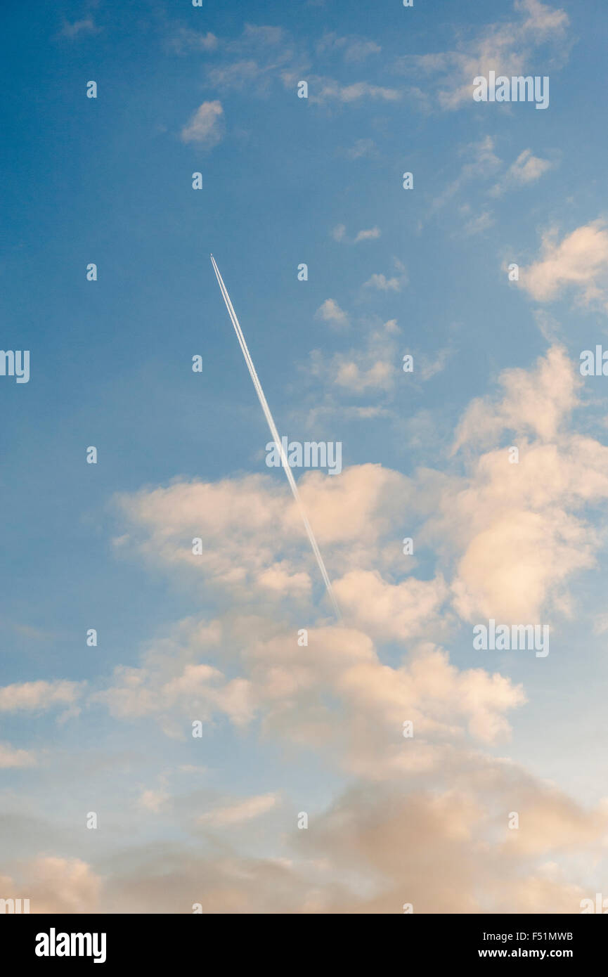 Piano e contrails e nuvole su un cielo blu Foto Stock