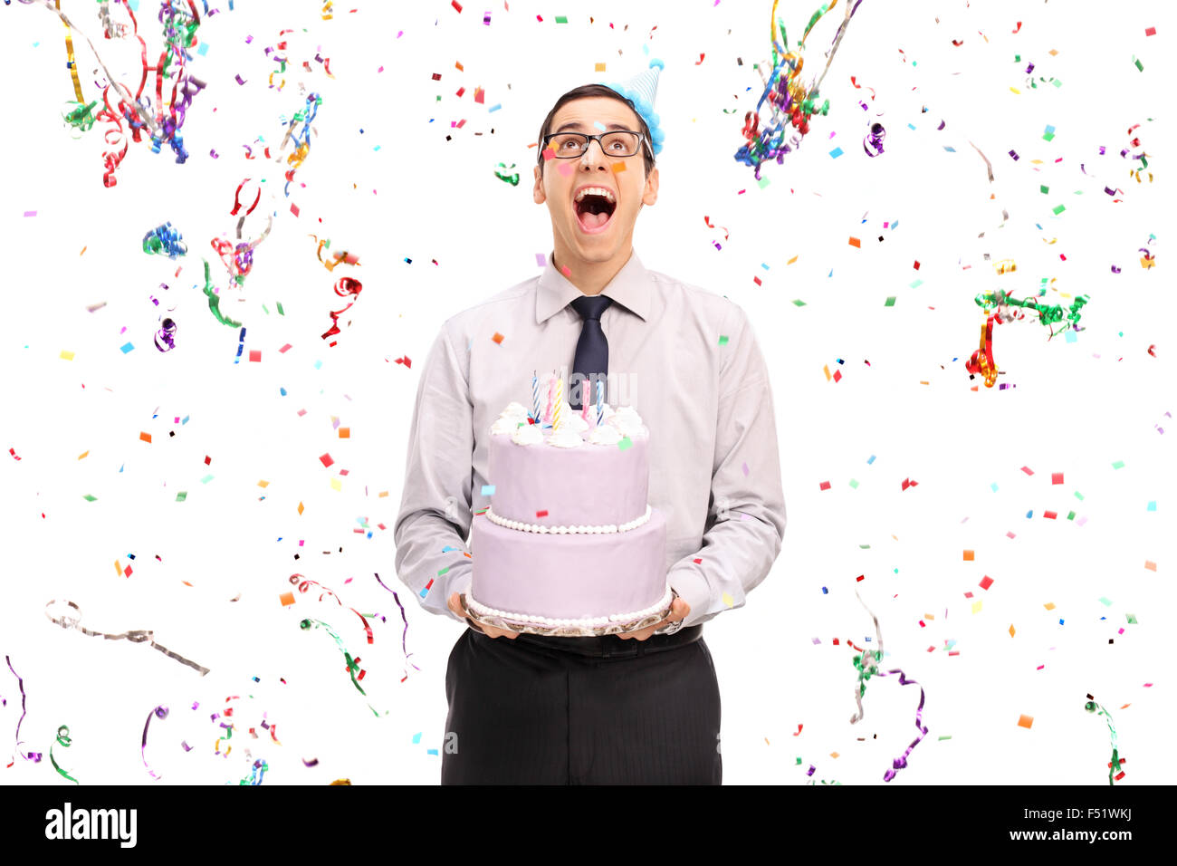 Studio shot di un lieto uomo con una torta di compleanno e guardando i confetti streamers battenti intorno a lui Foto Stock