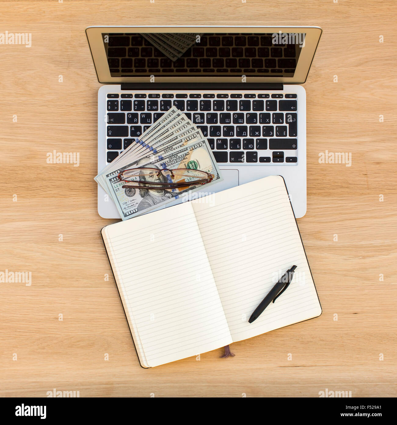 Laptop, notebook con una penna e le fatture del dollaro sulla luce di un tavolo di legno vista dall'alto. Foto Stock