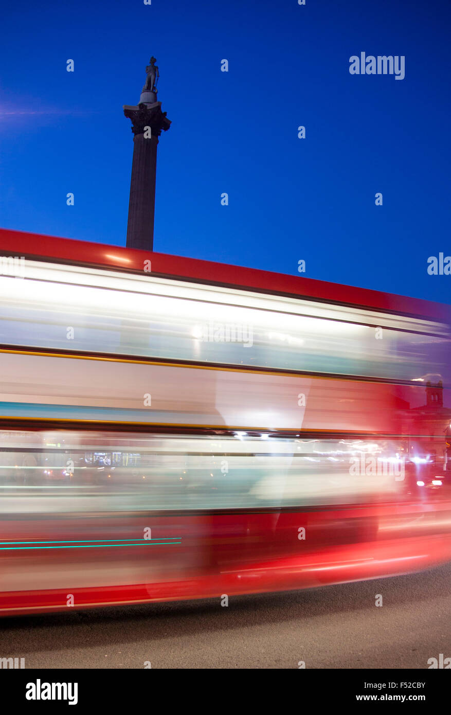 Red Bus londinese passando attraverso Trafalgar Square di notte la sfocatura in movimento con Nelson la colonna del background in Londra England Regno Unito Foto Stock