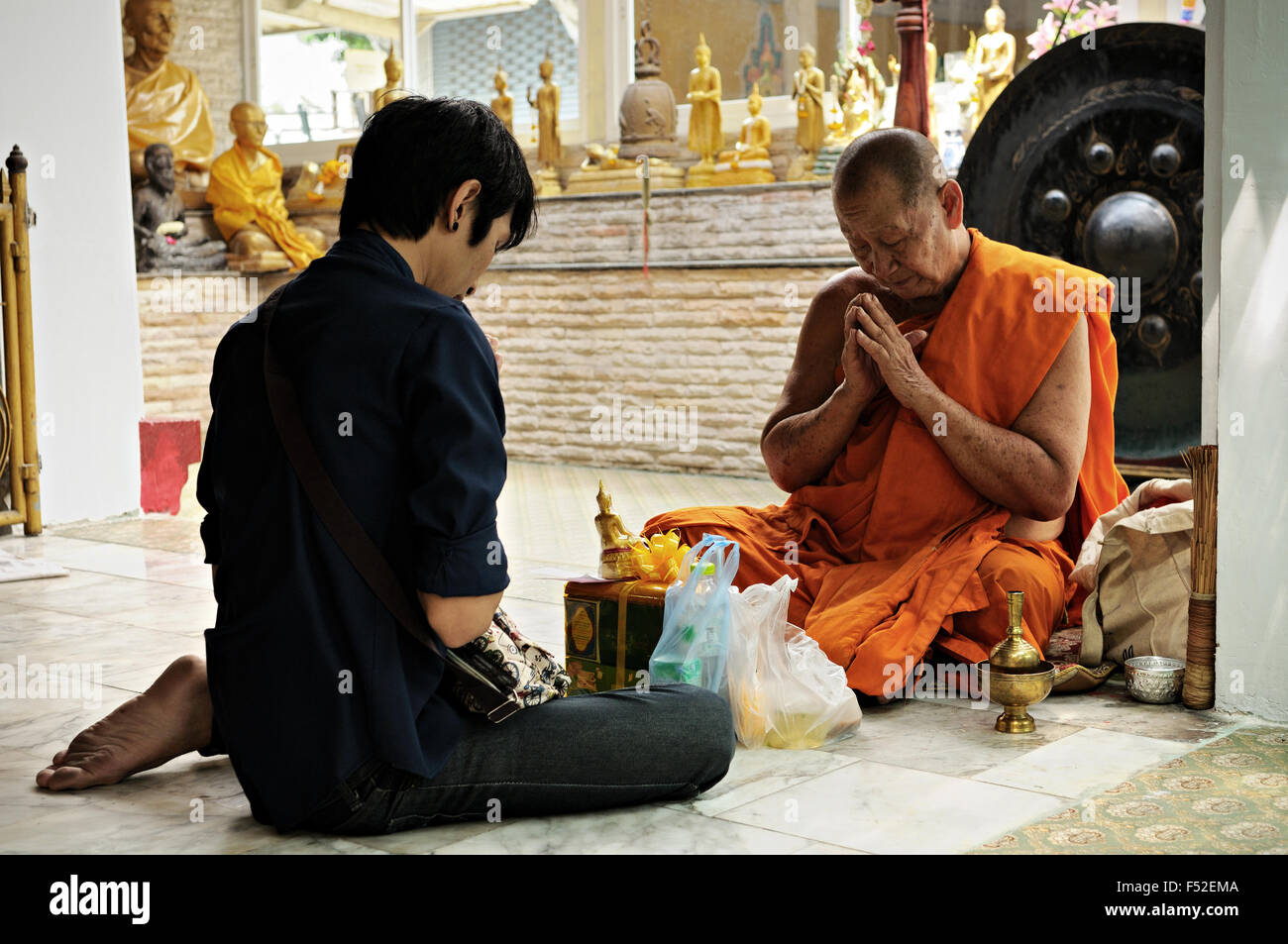 Giovane con un monaco seduto sul pavimento pregando presso Wat Sunthorn Thammathan, Bangkok, Thailandia Foto Stock