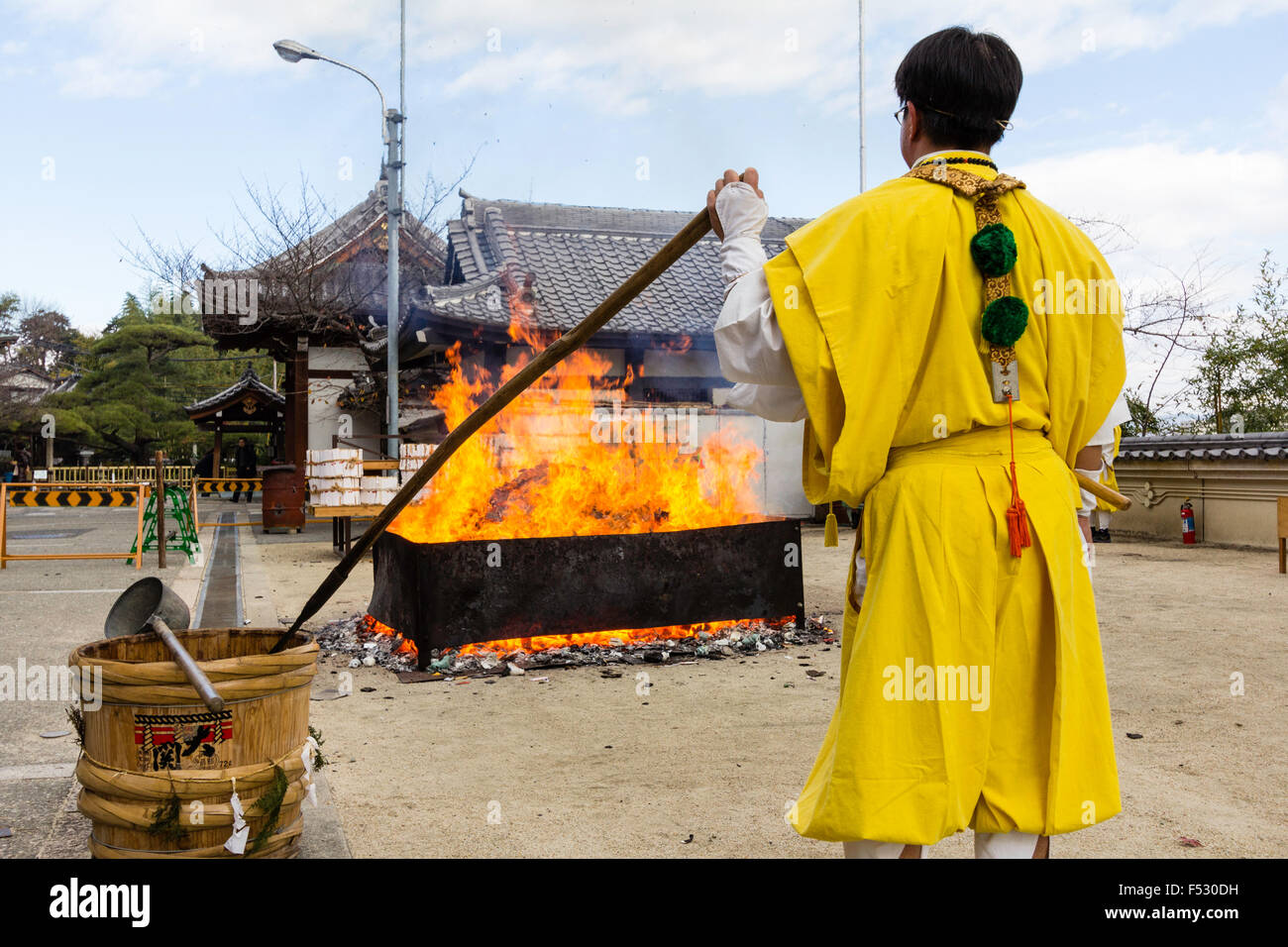 Giappone, Nishinomiya, Mondo Yakujin tempio buddista. Sacerdote in giallo Yamabushi accappatoi, in piedi a guardare il fuoco consuma l'anno di buona fortuna fascino. Foto Stock