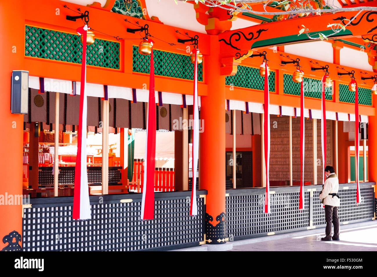 Kyoto, Fushimi Inari santuario. Vista lungo la parte anteriore del santuario, Honden, sala principale con campana corde appendere. Uomo che prega da tamagaki, la griglia di protezione. Foto Stock