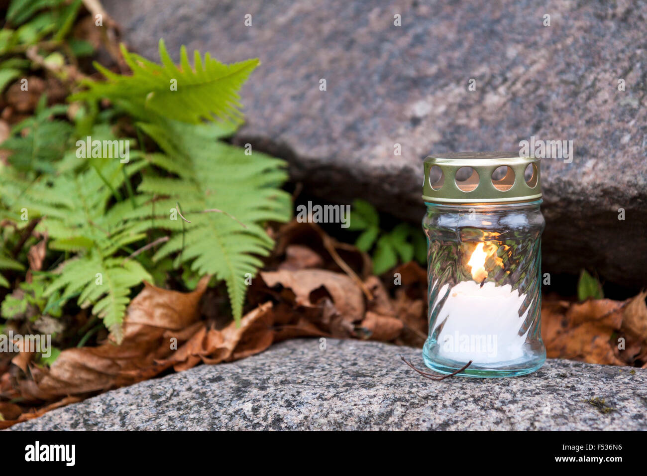 Lonely candela votiva sulla lapide e la masterizzazione. pietra tomba, piante verdi e impianti vecchi lascia visto in background poco profonda Foto Stock