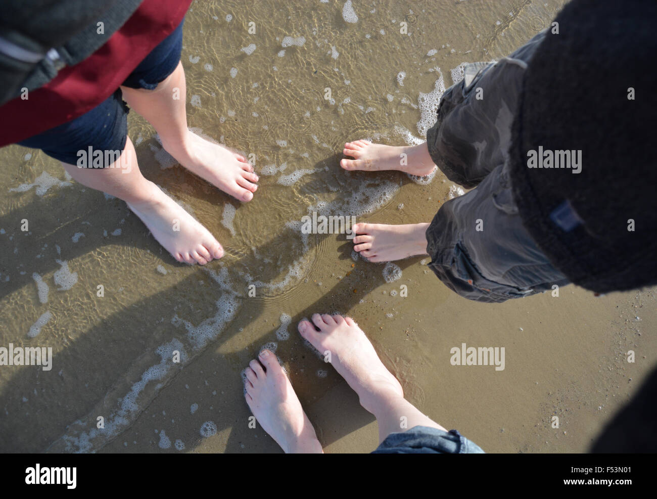Guardando verso il basso in corrispondenza di tre coppie di piedi sulla spiaggia al lato mare Foto Stock