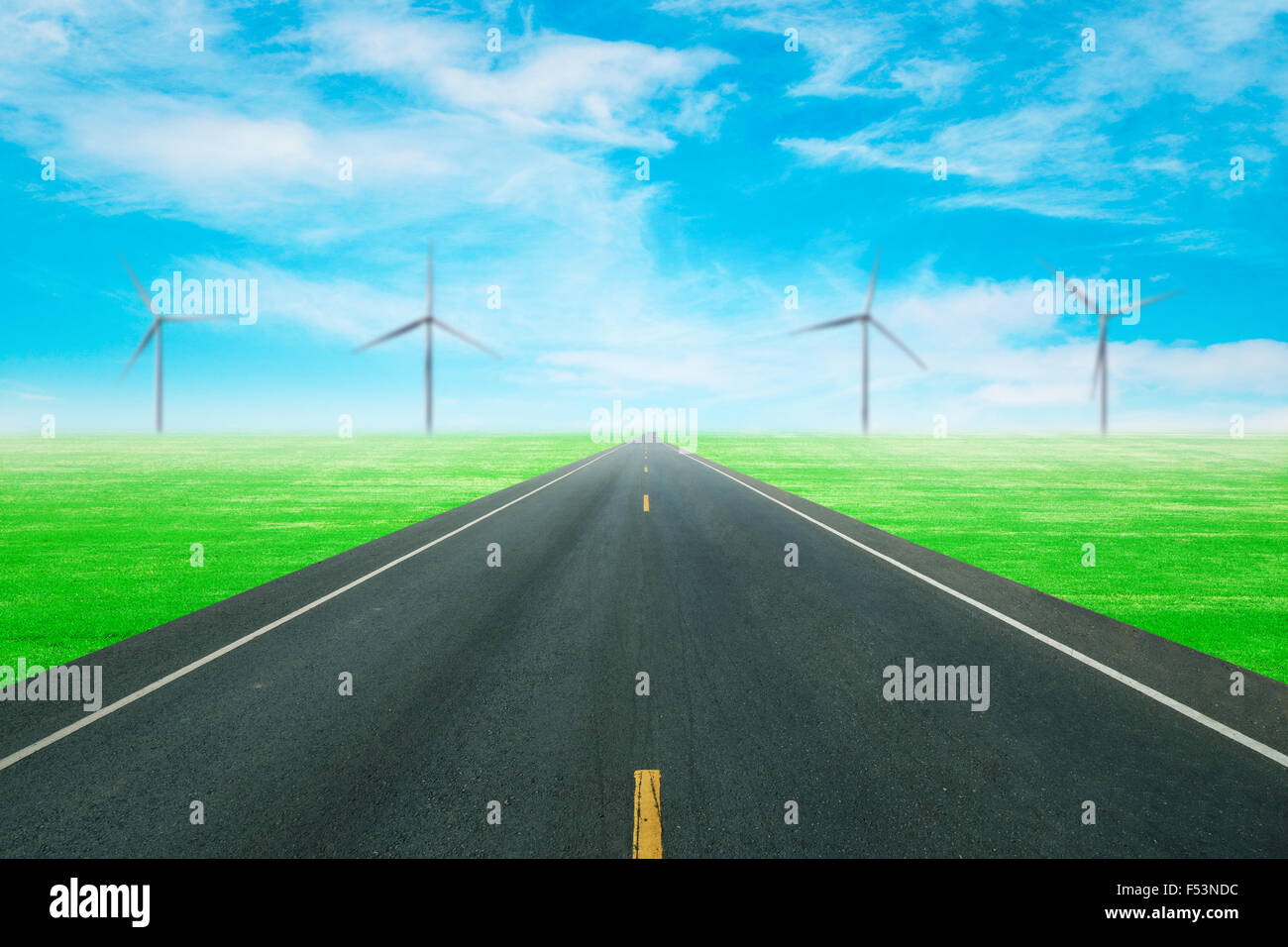 Strada asfaltata attraverso il campo verde con turbina a vento e cielo blu sullo sfondo Foto Stock