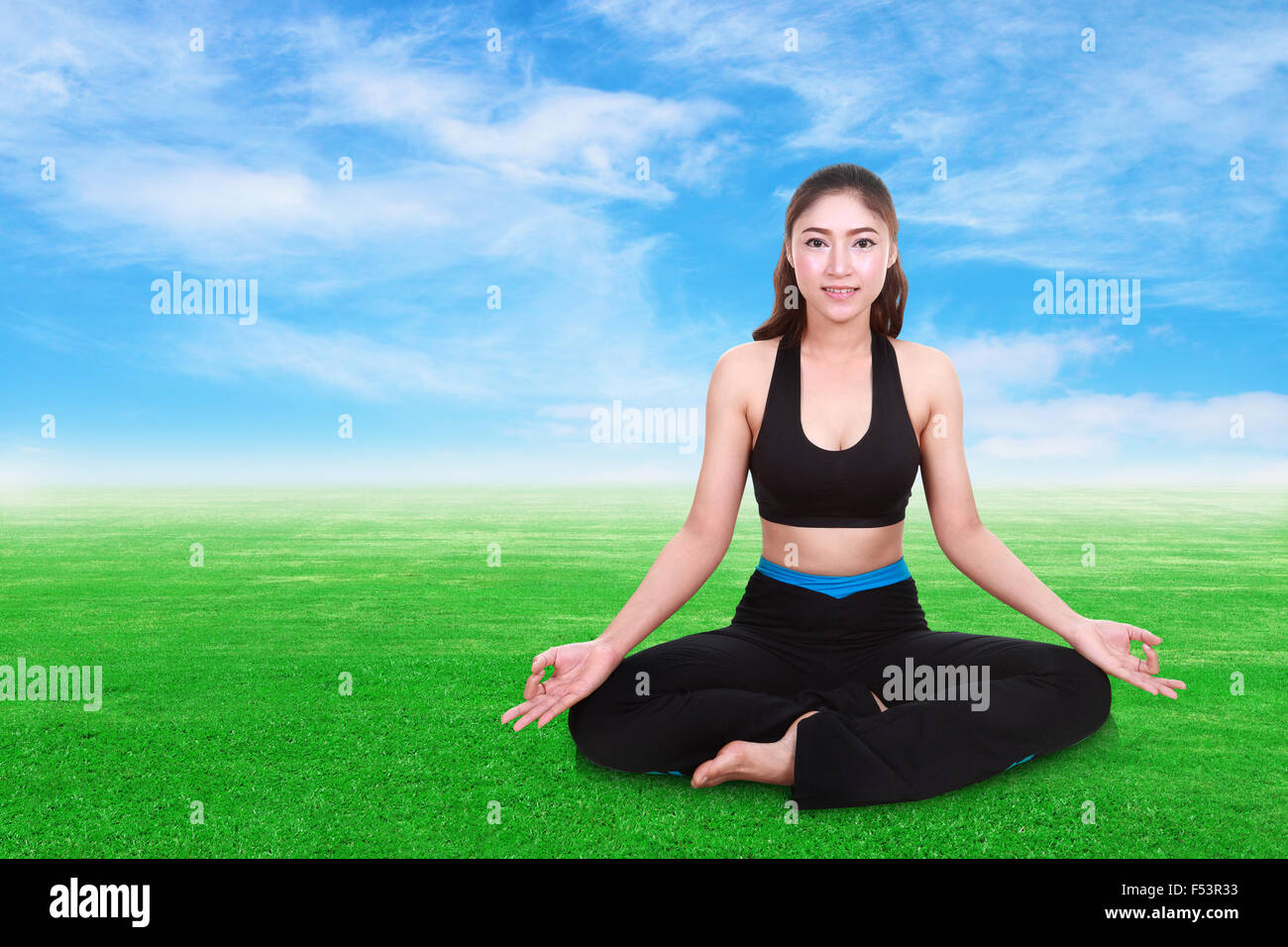 Giovane donna facendo esercizio di yoga su erba con sky Foto Stock