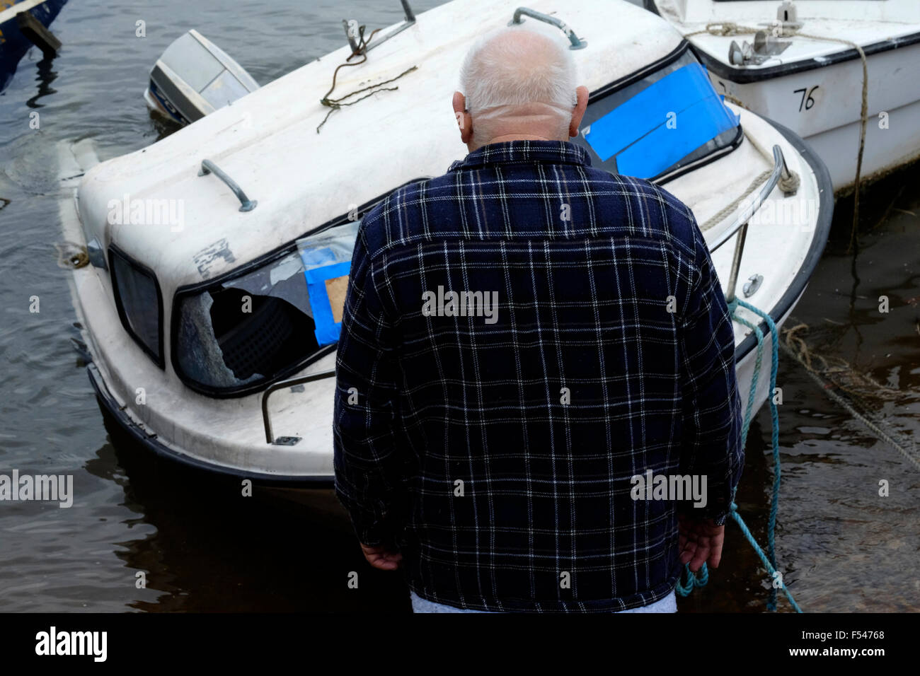 Uomo anziano guardando semi sommerso danneggiato barca nel porto di Portsmouth Inghilterra Regno Unito Foto Stock