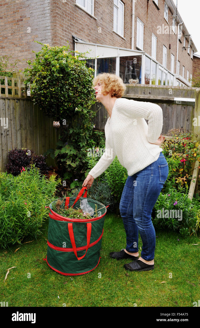 Donna matura il giardinaggio il sollevamento di un carico pesante sacchetto di rifiuti del giardino nel dolore con un brutto mal di schiena Foto Stock