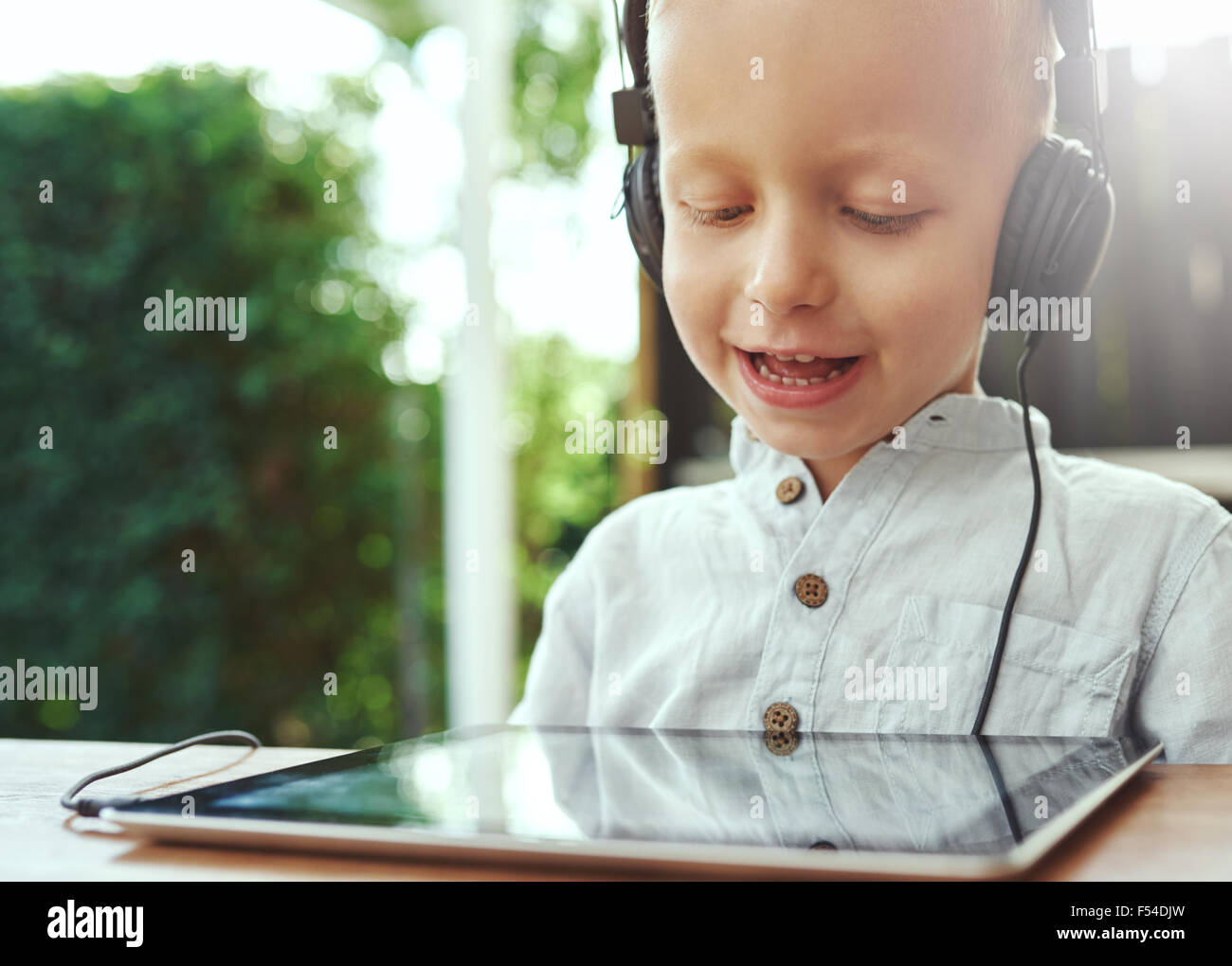 Adorable little boy ascoltando la musica registrata sul suo computer tablet utilizzando le cuffie con un delizioso sorriso di contentezza un Foto Stock