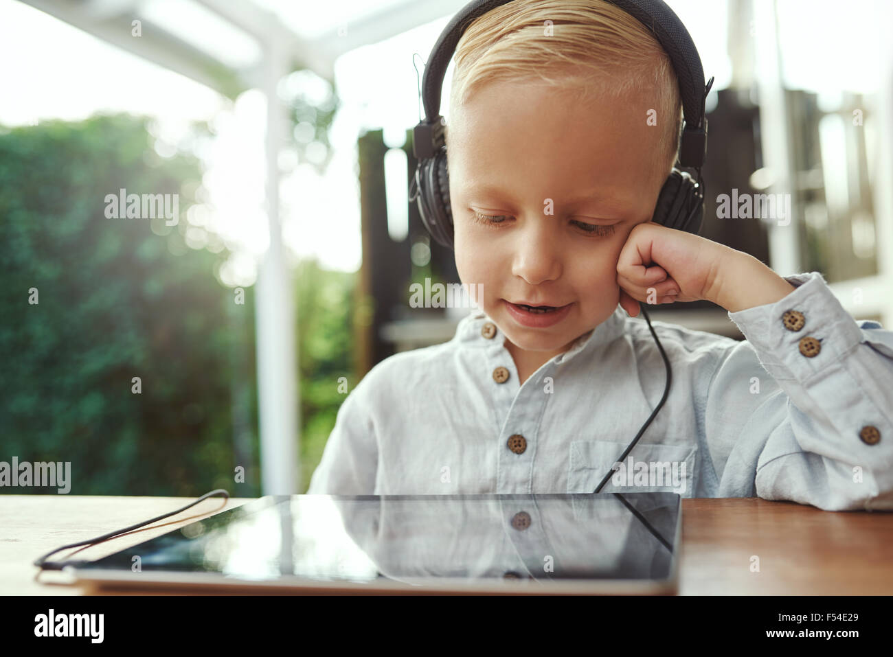 Adorable del giovane ragazzo seduto con un computer tablet ascoltando la sua libreria musicale con un sorriso di contentezza su un set di s Foto Stock