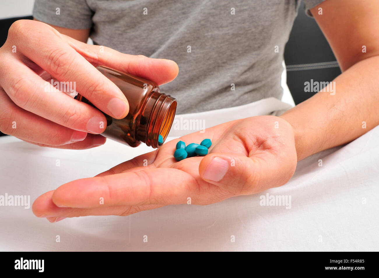 Un giovane uomo caucasico in pigiama nel letto in procinto di prendere alcune pillole blu da una bottiglia marrone Foto Stock