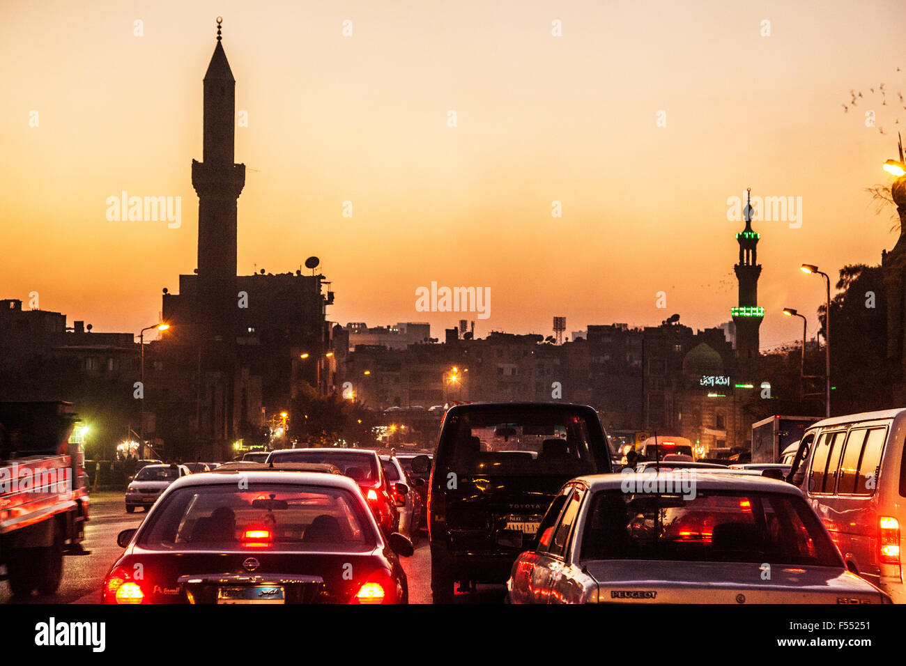 Il traffico del Cairo al tramonto con due minareti stagliano contro un cielo d'oro. Foto Stock