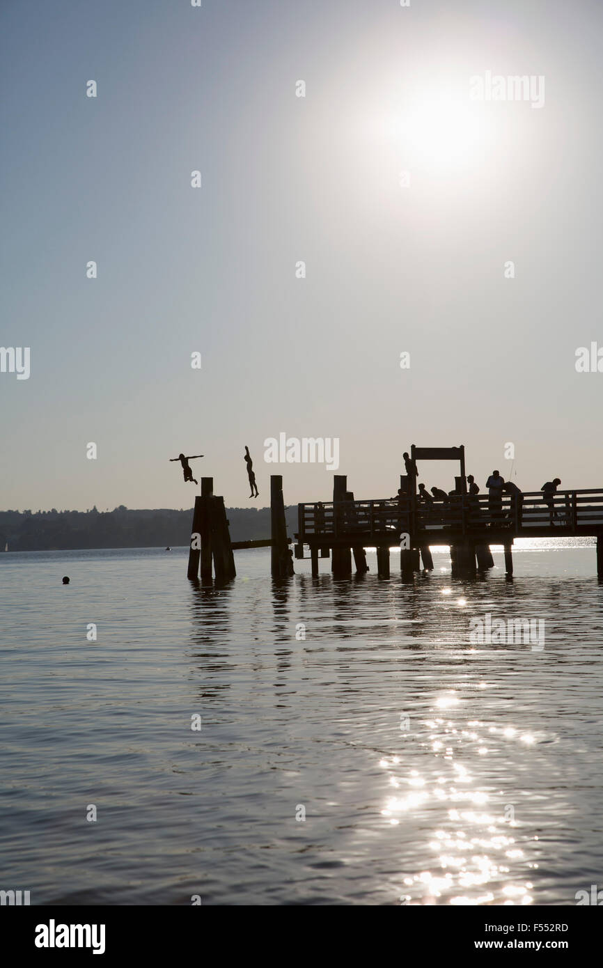Silhouette Persone che saltano nel lago contro il cielo al tramonto Foto Stock