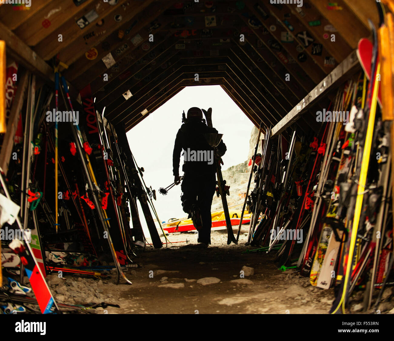 Vista posteriore dell'uomo con attrezzature da sci passeggiate fuori del capannone Foto Stock