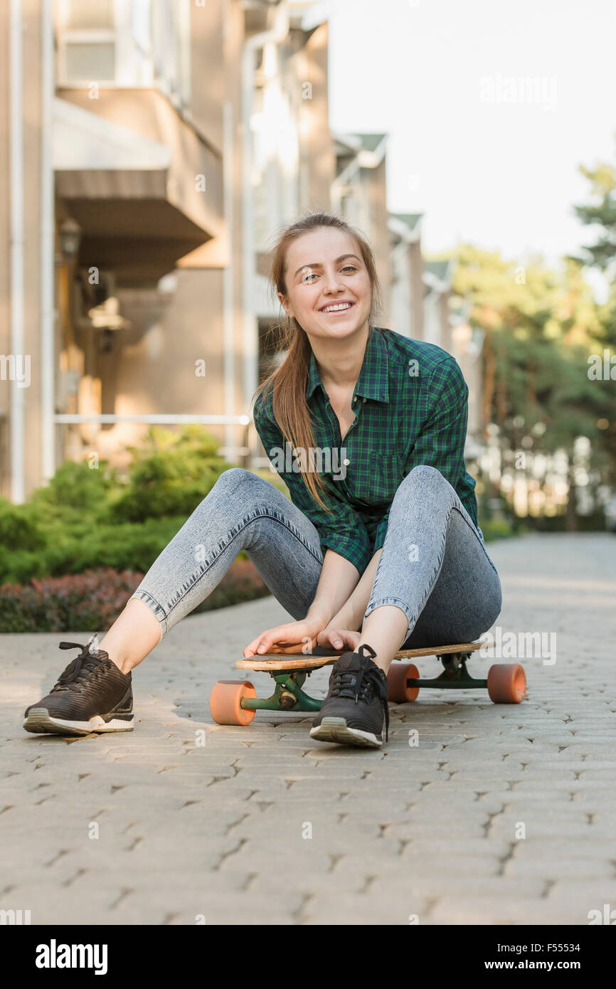 Ritratto di felice giovane donna seduta su skateboard all'aperto Foto Stock