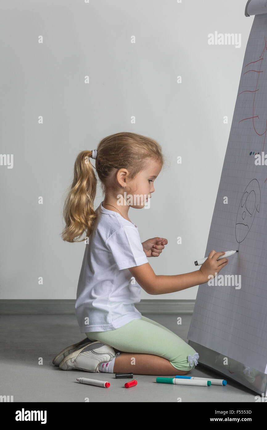 Vista laterale della ragazza inginocchiarsi durante il disegno sulla lavagna a fogli mobili contro il muro bianco Foto Stock