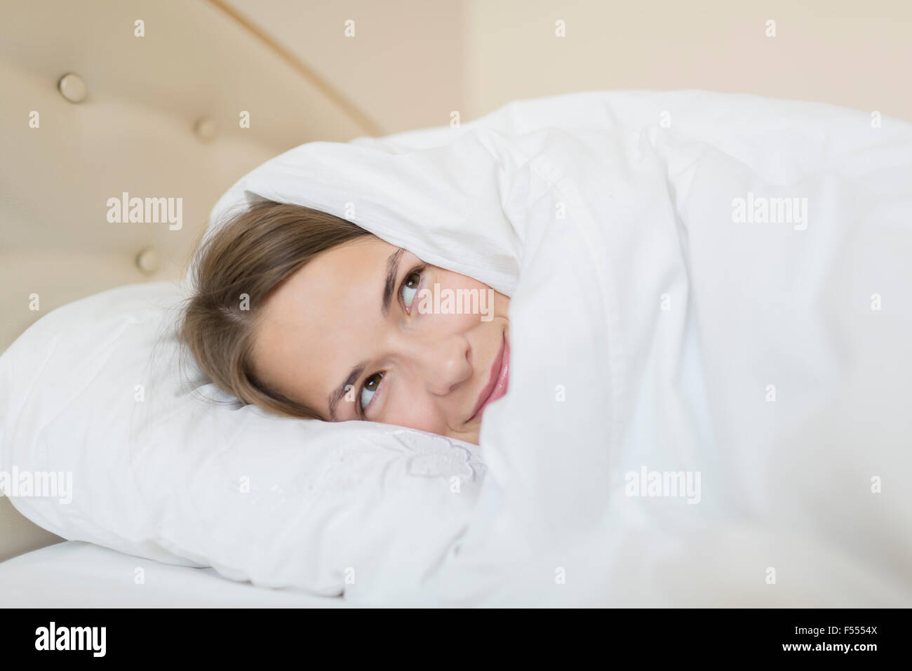 Premurosa donna coperta con piumone che guarda lontano mentre vi rilassate nel letto di casa Foto Stock
