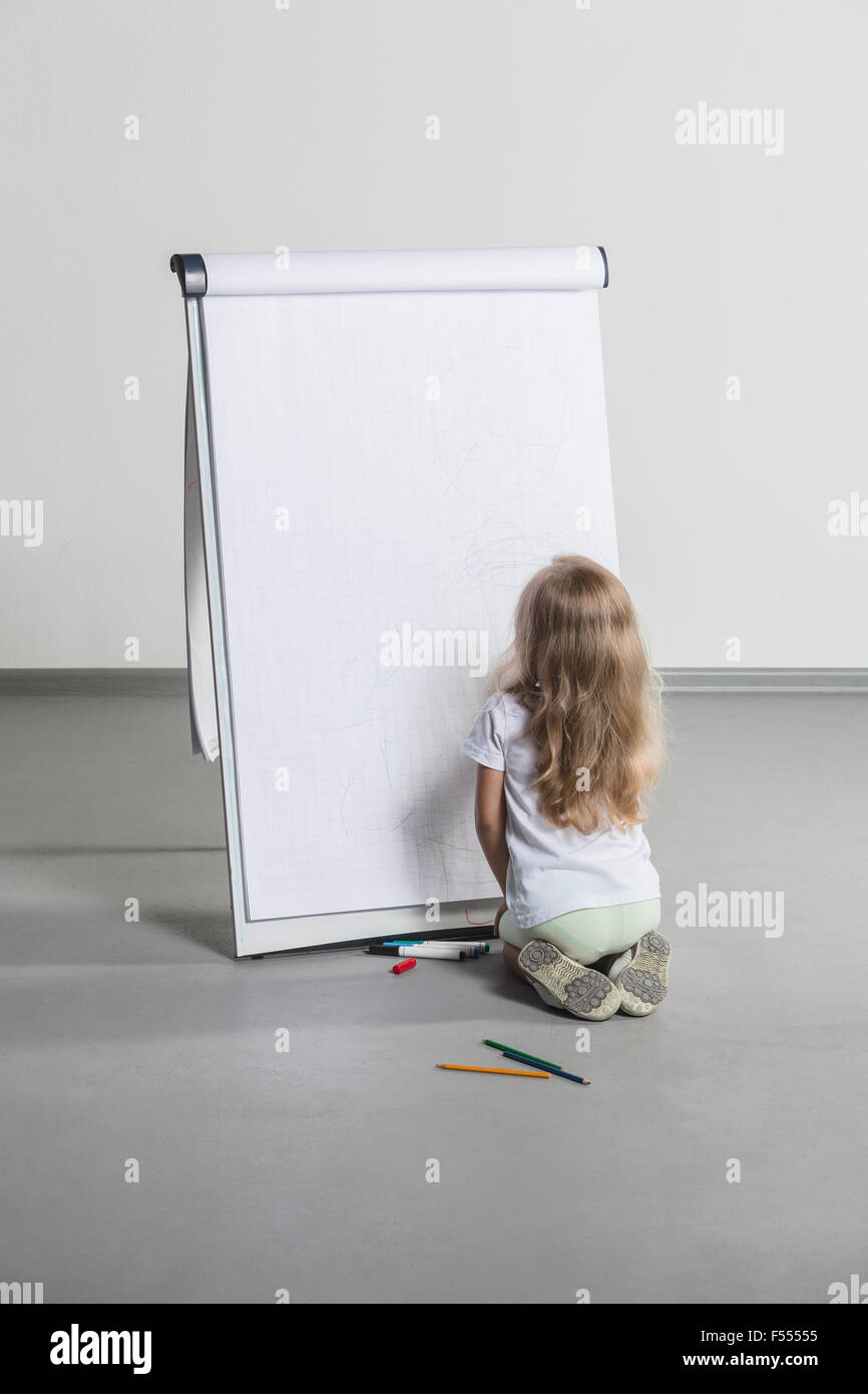 Vista posteriore di una ragazza disegno sulla lavagna a fogli mobili contro il muro bianco Foto Stock