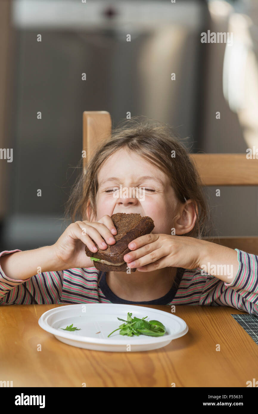 Ragazza carina mangiare panino a tavola in casa Foto Stock