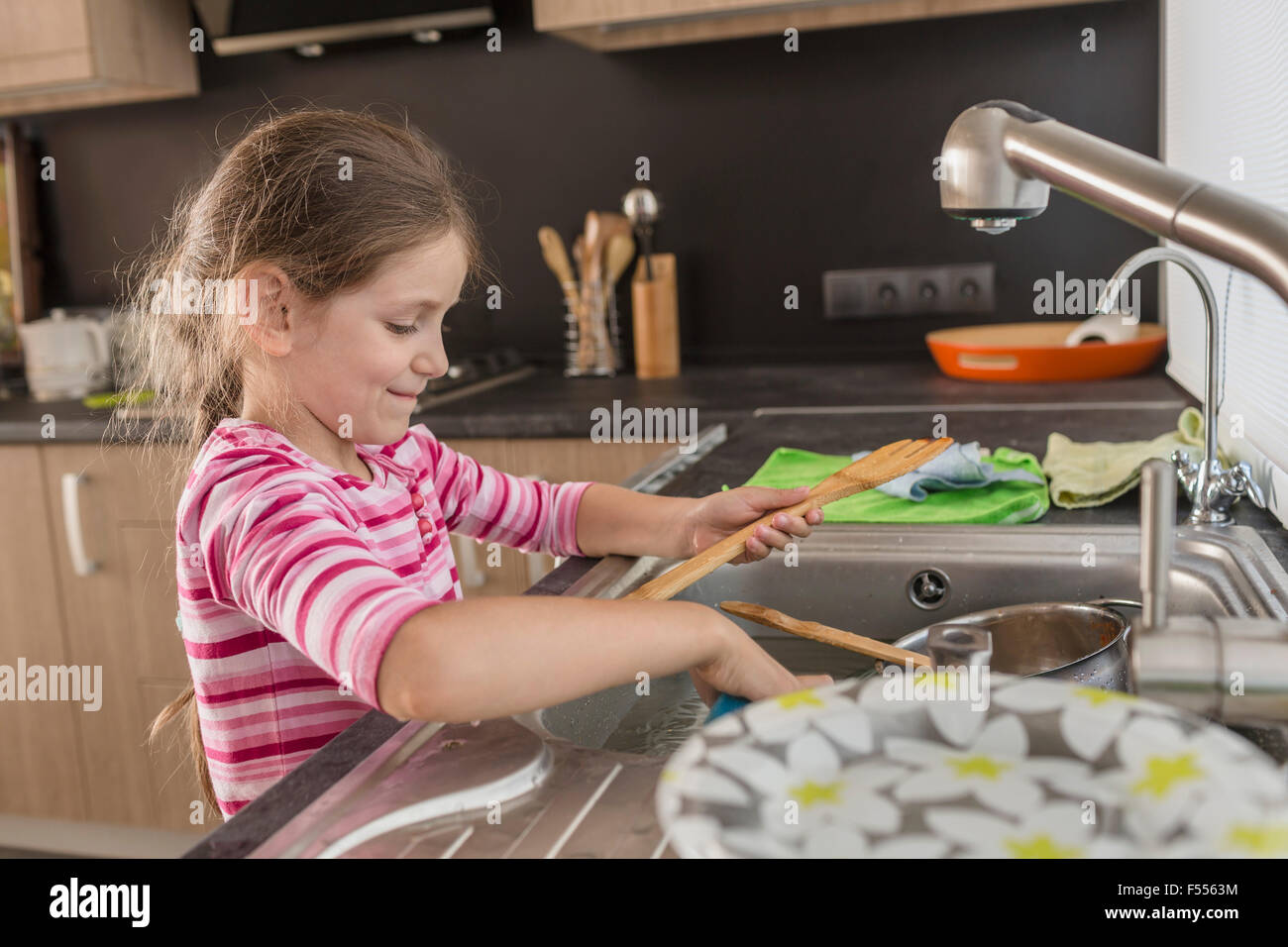 Ragazza sorridente il lavaggio di utensili in cucina a casa Foto Stock