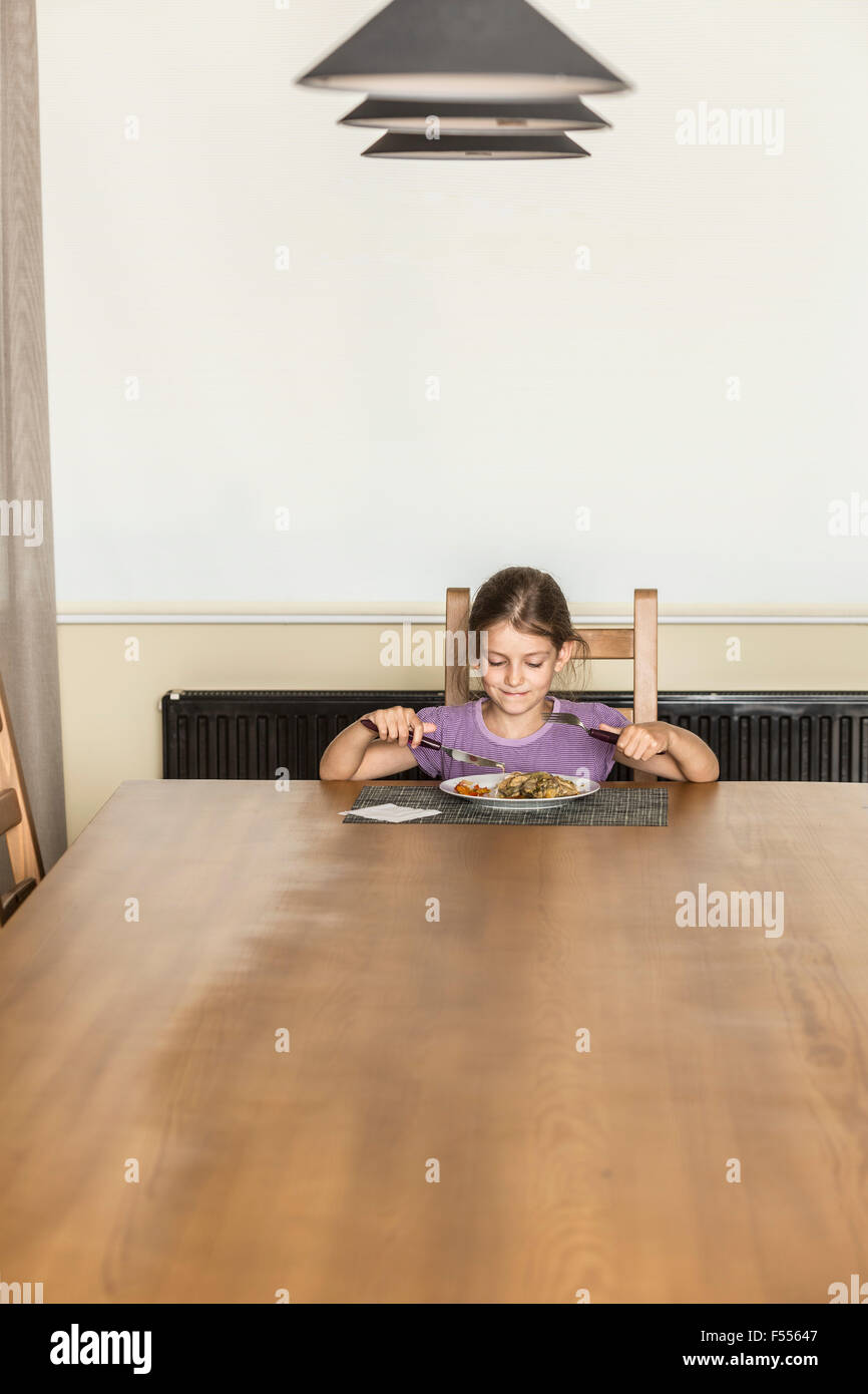 Ragazza avente il cibo al tavolo da pranzo in casa Foto Stock