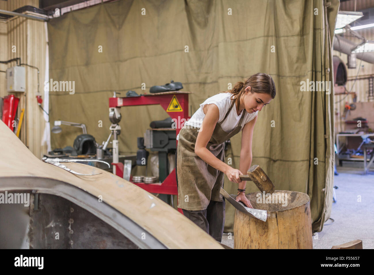 Meccanico femmina colpendo metallico sul barile di legno al garage Foto Stock
