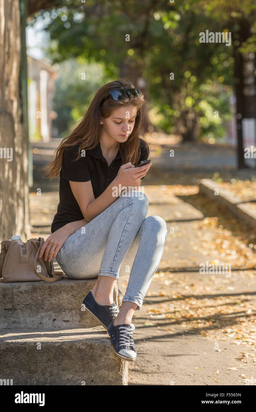 Donna che utilizza smart phone mentre è seduto sui gradini esterni Foto Stock