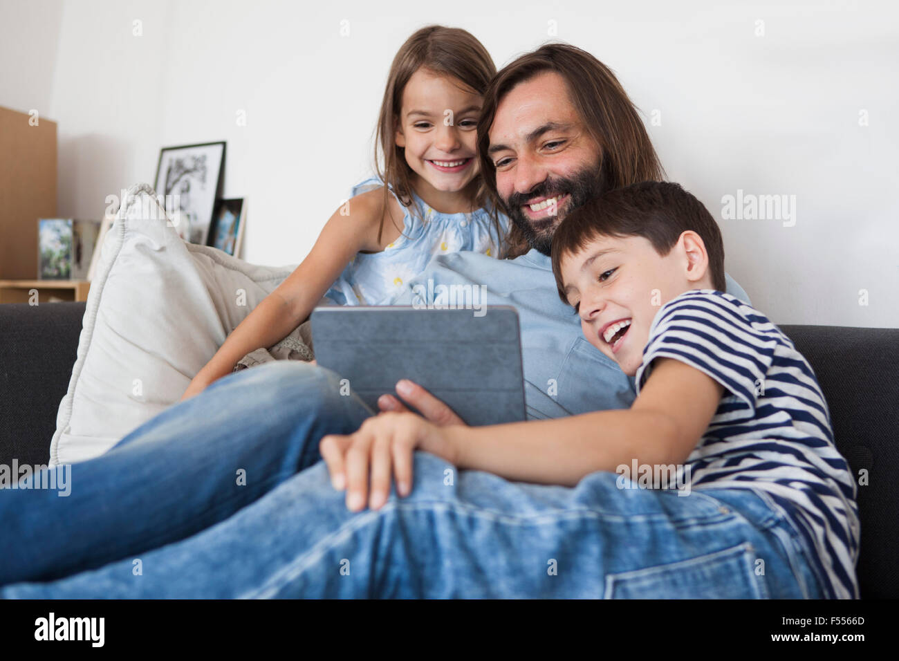 Padre Felice con bambini con tavoletta digitale sul divano di casa Foto Stock