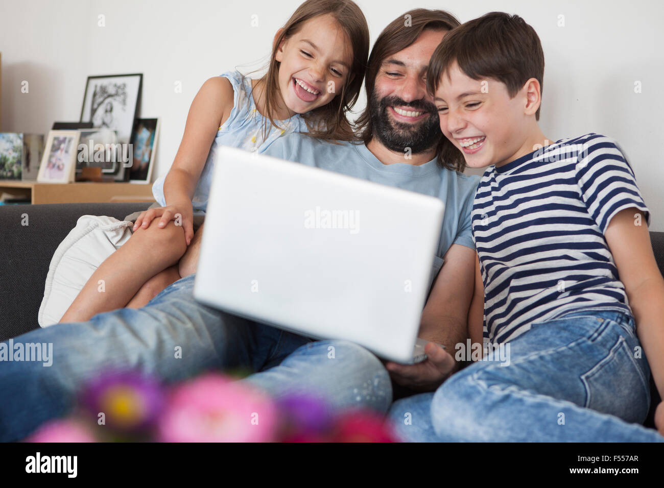 Allegro padre con i bambini utilizzando computer portatile sul divano di casa Foto Stock