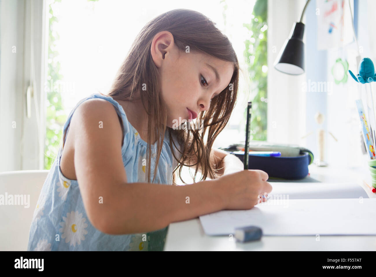 Vista laterale della ragazza iscritto nel libro sul tavolo a casa Foto Stock