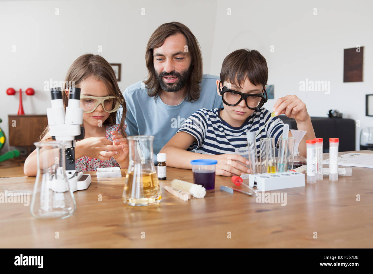 Padre ad assistere i bambini nel fare la scienza a scuola progetto a casa Foto Stock