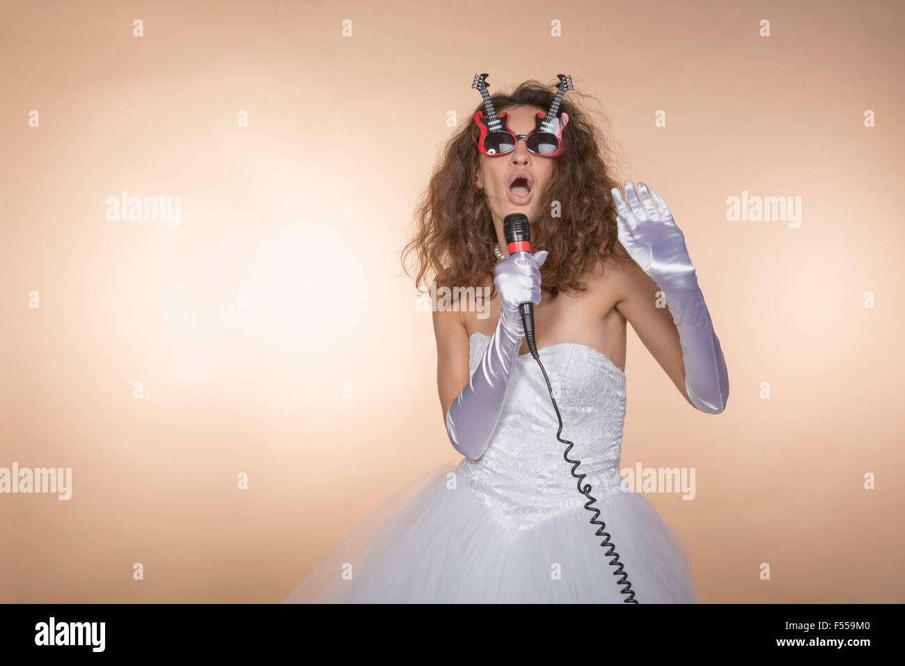 Eccitato in sposa a forma di chitarra bicchieri cantando contro sfondo colorato Foto Stock