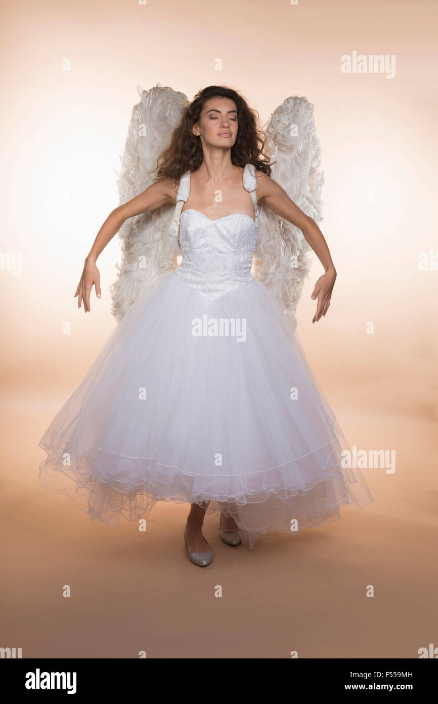 Sposa con gli occhi chiusi indossando ali d'angelo mentre in piedi contro sfondo colorato Foto Stock