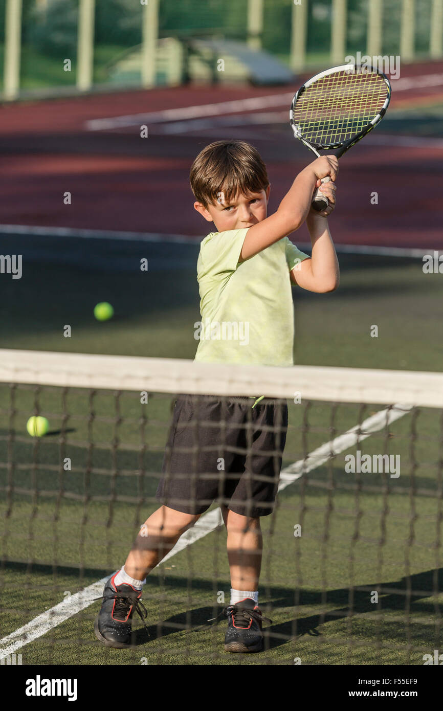 Ragazzo giocando a tennis in tribunale durante la giornata di sole Foto Stock
