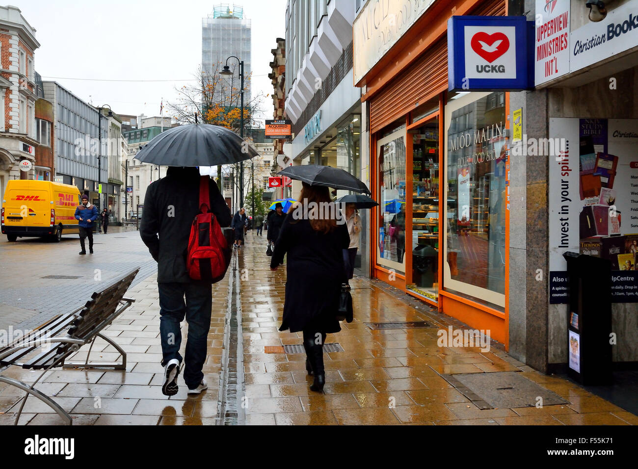 Un uomo e una donna a piedi sotto la pioggia con ombrelloni a Luton, Bedfordshire, Inghilterra Foto Stock
