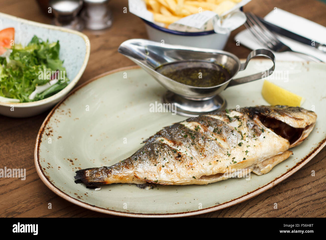 Tutto alla griglia branzino con insalata e la porzione di chip Foto Stock