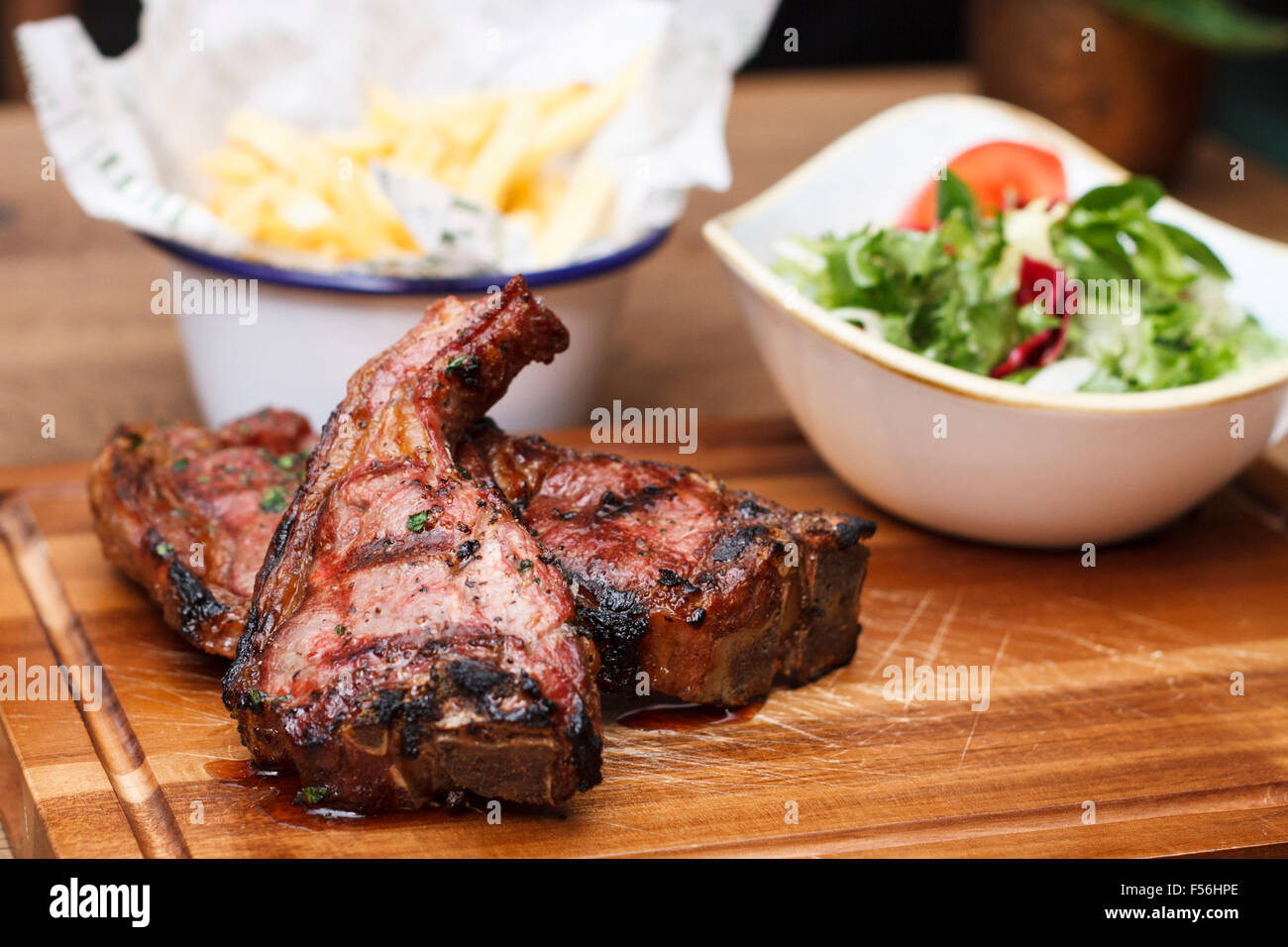 Costolette di agnello grigliate su un tagliere di legno con una porzione di insalata e patatine fritte Foto Stock