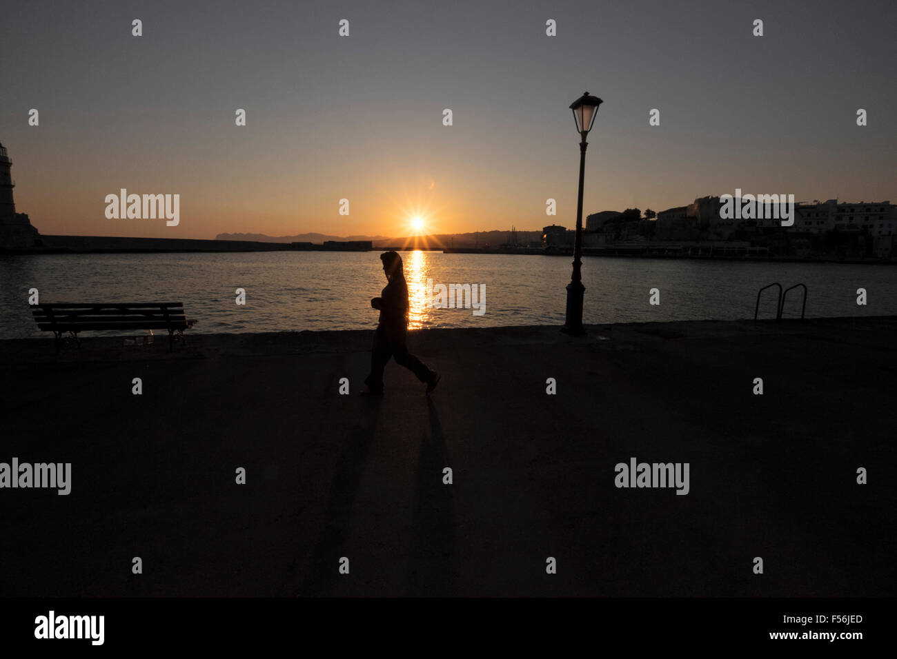 Una giovane donna cammina lungo il Porto Veneziano waterfront presso sunrise a Chania sull isola di Creta in Grecia Foto Stock