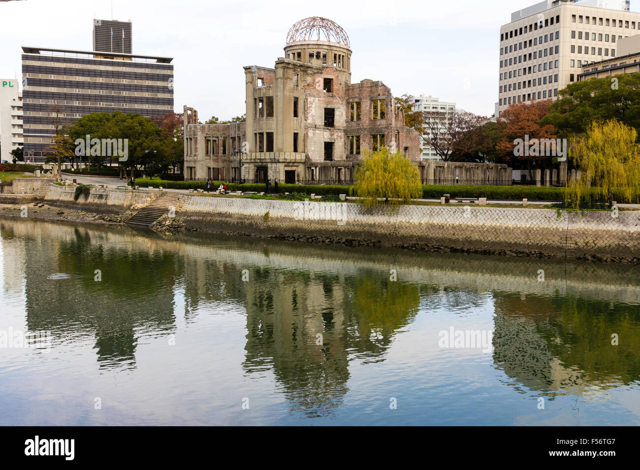 Giappone, Hiroshima. La cupola della bomba atomica, il Genbaku Dōmu, memorial con un moderno ufficio blocchi dietro e il fiume Honkawa in primo piano. Foto Stock