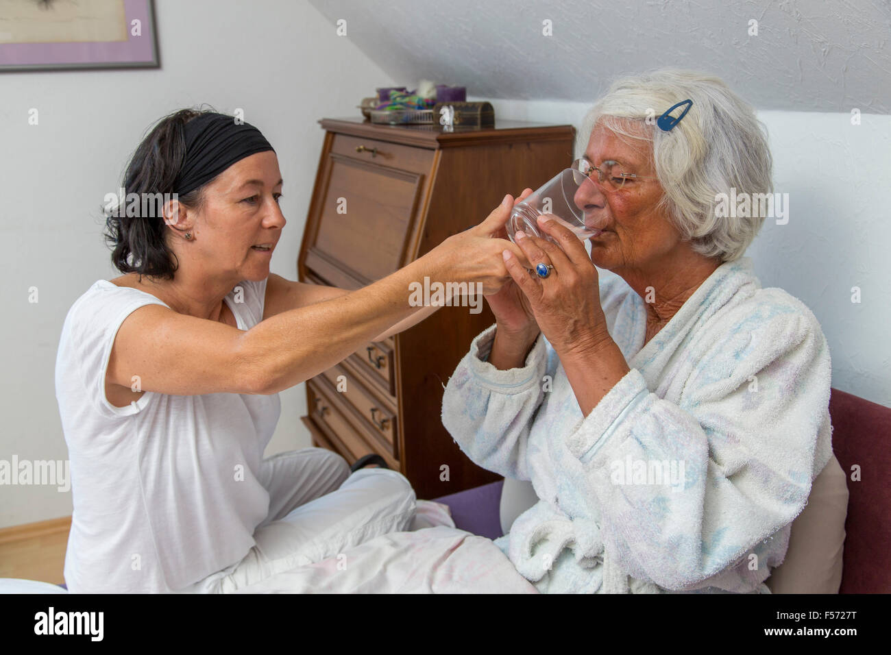 Assistenza agli anziani a casa, infermiere di cure per una donna anziana, contribuendo con un bicchiere di acqua, Foto Stock