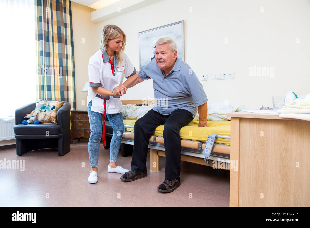 Assistenza agli anziani in una casa di cura, infermiere aiuta un anziano uomo di alzarsi dal letto, Foto Stock