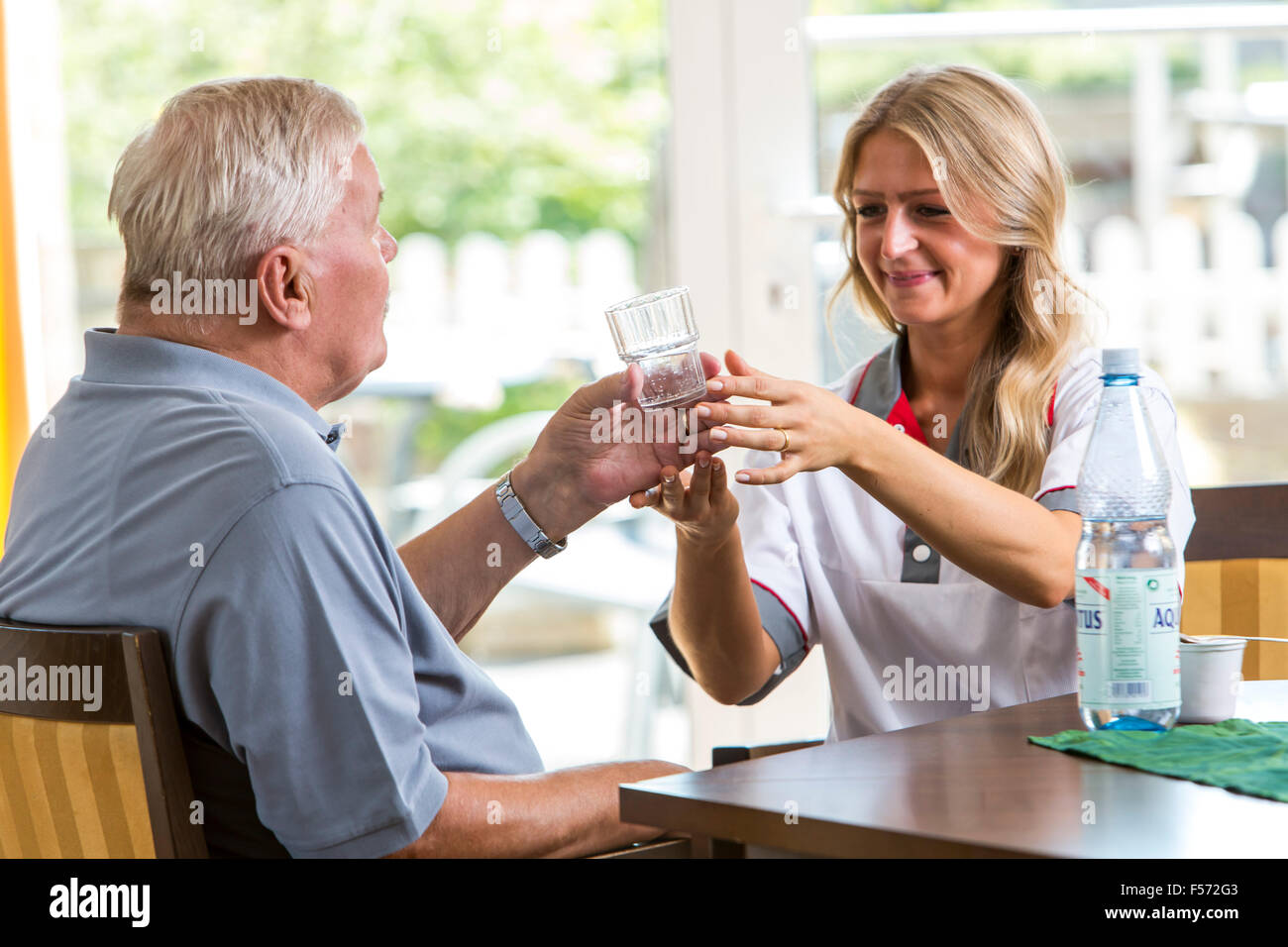 Assistenza agli anziani in una casa di cura, infermiere aiuta un uomo anziano bere un bicchiere d'acqua, Foto Stock