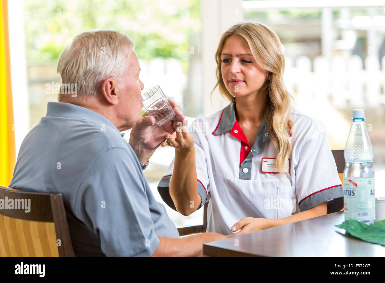 Assistenza agli anziani in una casa di cura, infermiere aiuta un uomo anziano bere un bicchiere d'acqua, Foto Stock