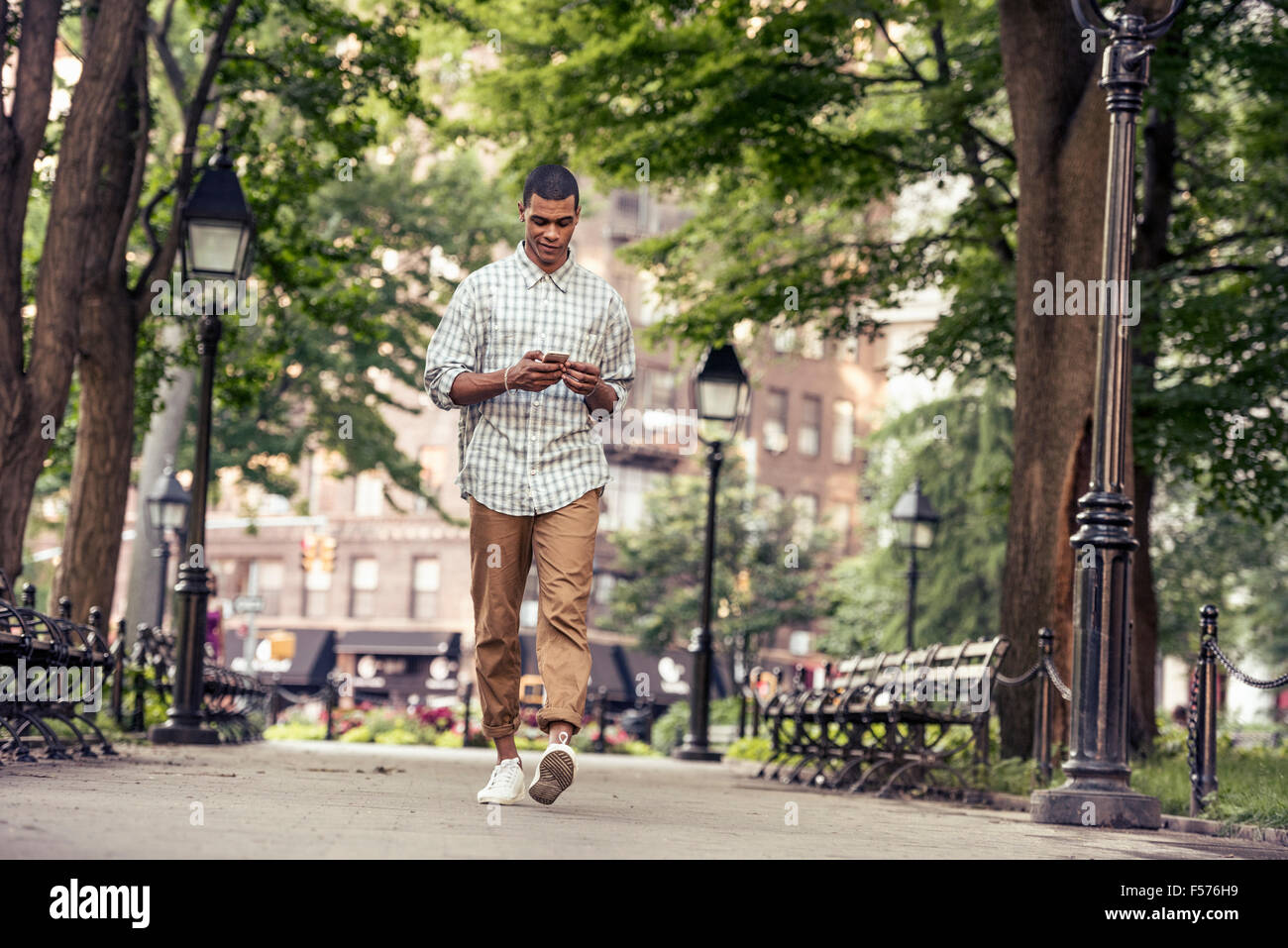 Un uomo a piedi attraverso una piazza cittadina guardando al suo smart phone Foto Stock