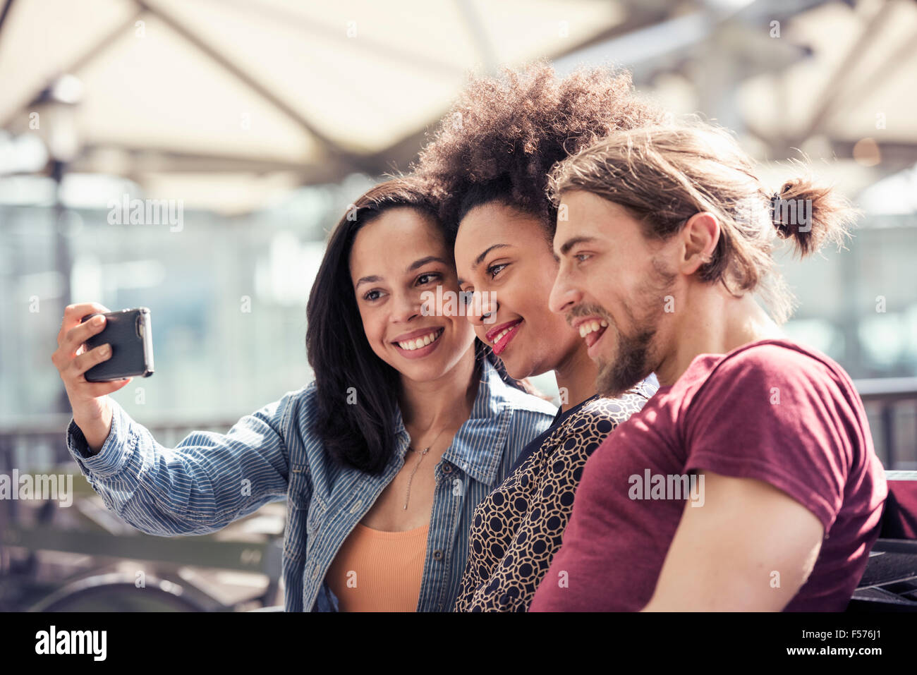 Tre persone, un uomo e due donne, tenendo selfies in un parco della città Foto Stock