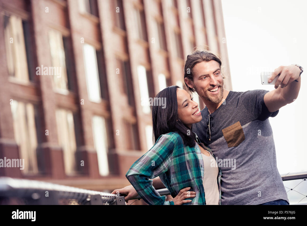 Un giovane uomo e donna prendendo un selfie da un grande edificio nella città Foto Stock